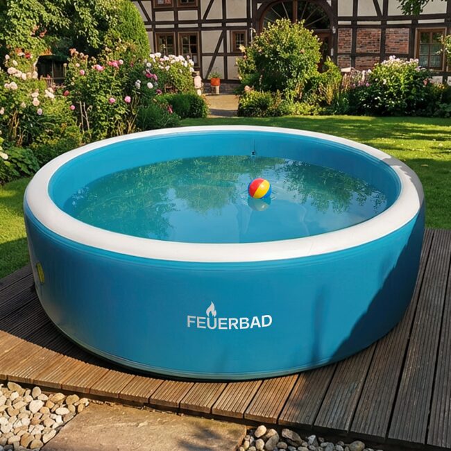 Außenansicht eines runden, aufblasbaren Pools von Feuerbad mit blauer Außenwand und klarem Wasser, platziert auf einer Holzterrasse in einem gepflegten Garten mit Rasen, Blumenbeeten und einem Fachwerkhaus im Hintergrund.