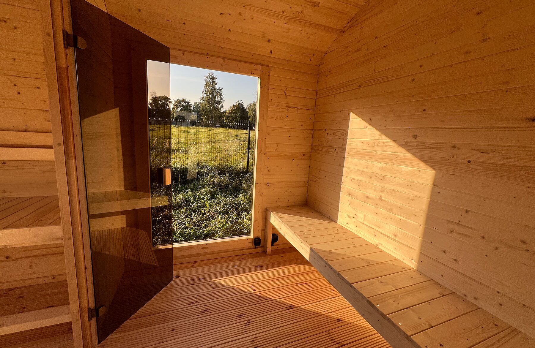 Innenansicht der Feuerbad Sauna CERES mit heller Holzverkleidung, integrierter Sitzbank und Glastür