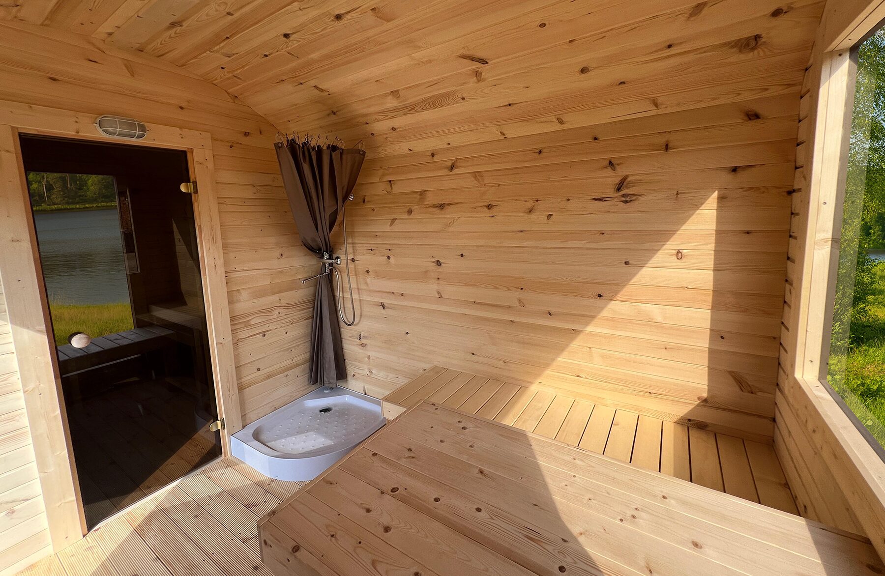 Innenansicht der Feuerbad Sauna CERES mit heller Holzverkleidung, integrierter Sitzbank, Dusche und Glastür
