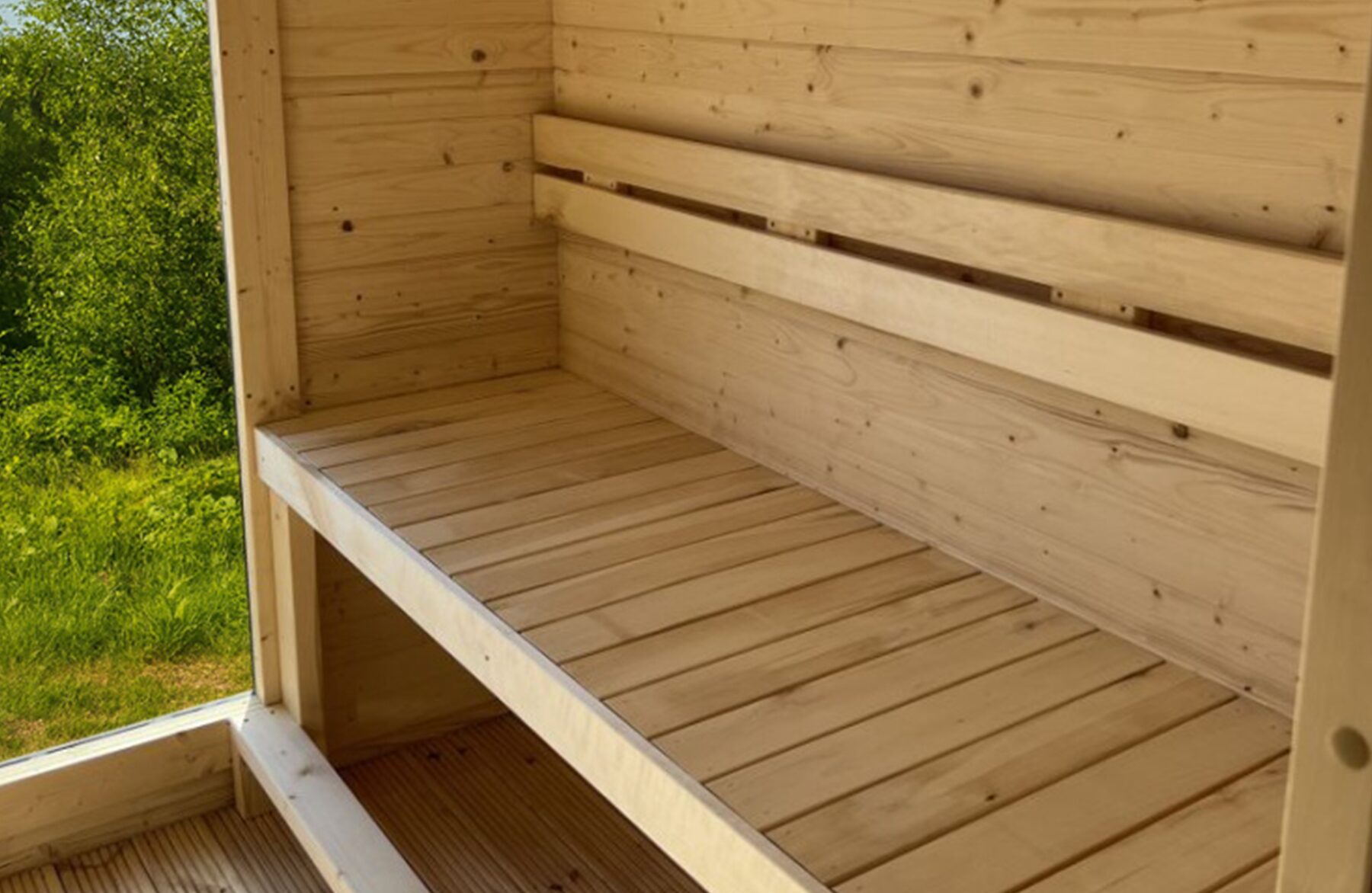 Innenansicht der Feuerbad Sauna CERES mit heller Holzverkleidung, integrierter Sitzbank und Fenster