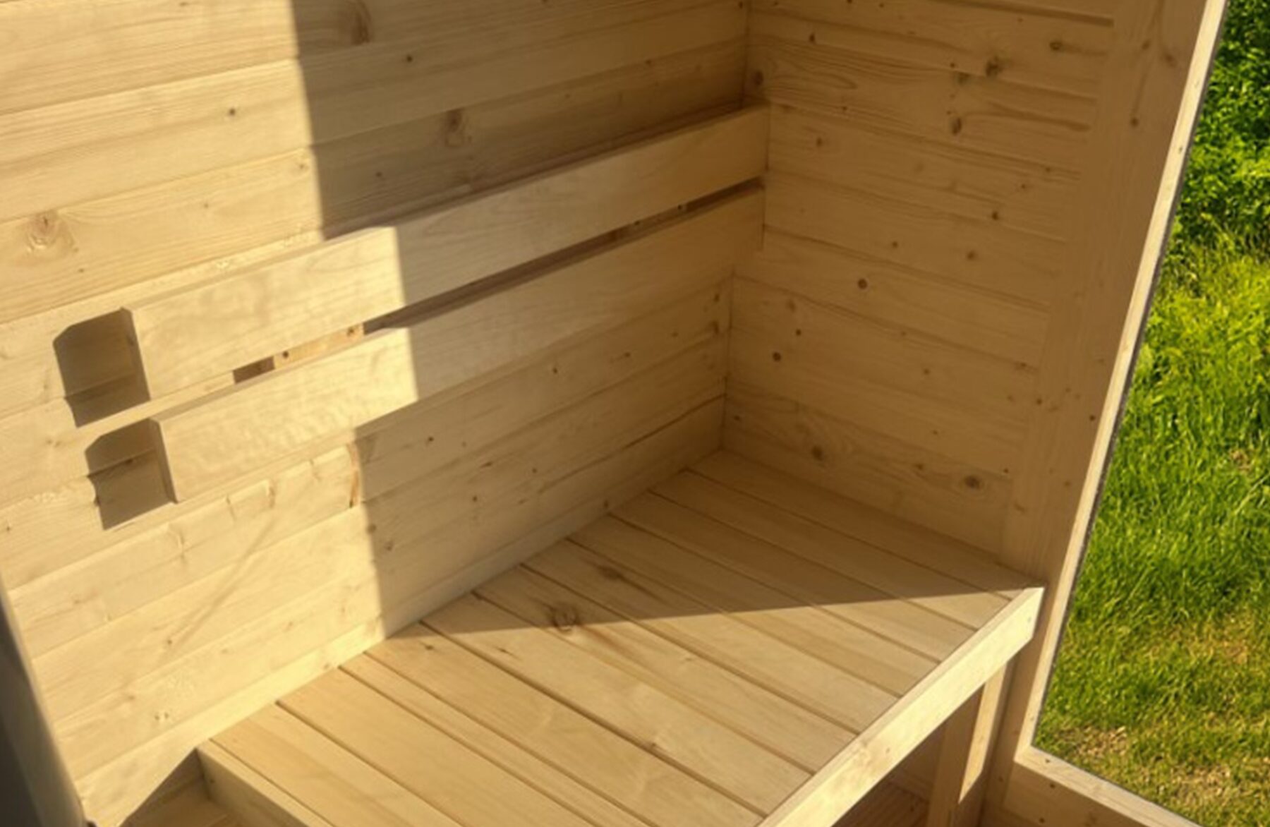 Innenansicht der Feuerbad Sauna CERES mit heller Holzverkleidung, integrierter Sitzbank und Fenster